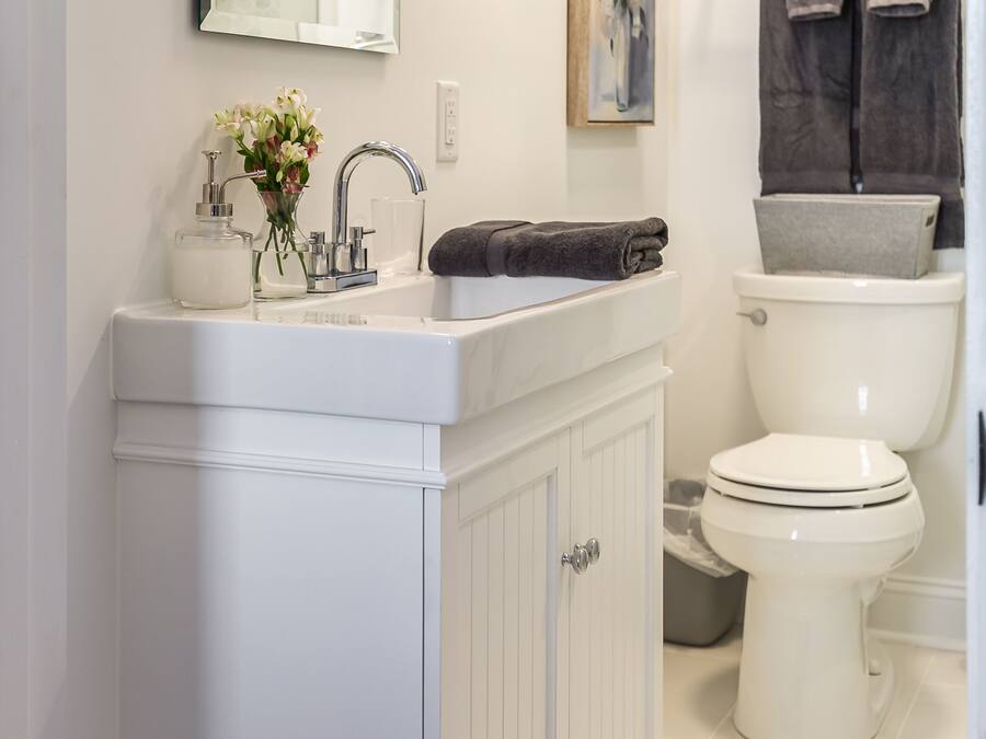 Ein Badezimmer mit weißem Waschtisch, Waschbecken, Spiegel, Toilette und zwei Handtüchern an einem Wäscheständer.