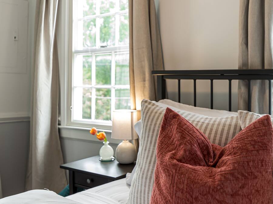 A bedroom with a bed, a nightstand, a lamp, and a window with curtains.