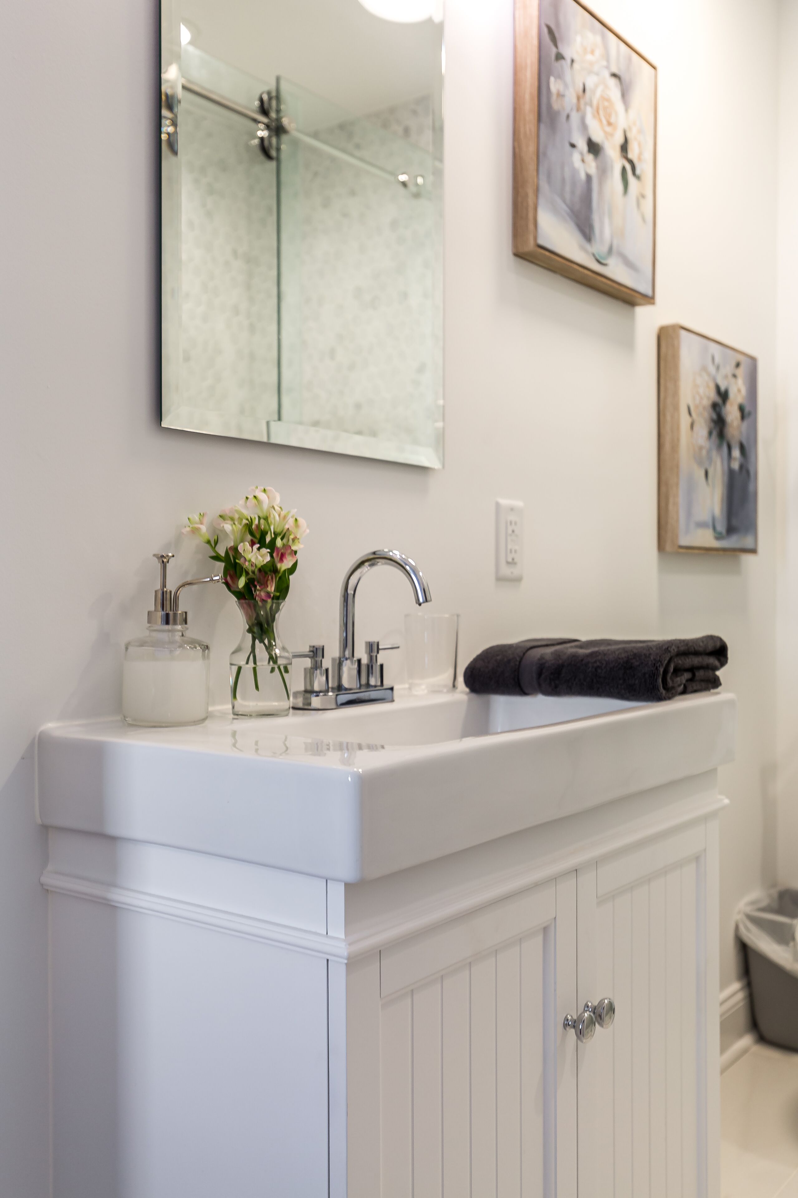 A bathroom with a white vanity, a mirror, a sink, a towel, and a trash can.