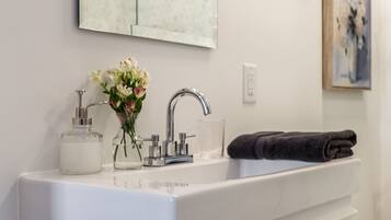 A bathroom with a white vanity, a mirror, a sink, a towel, and a trash can.
