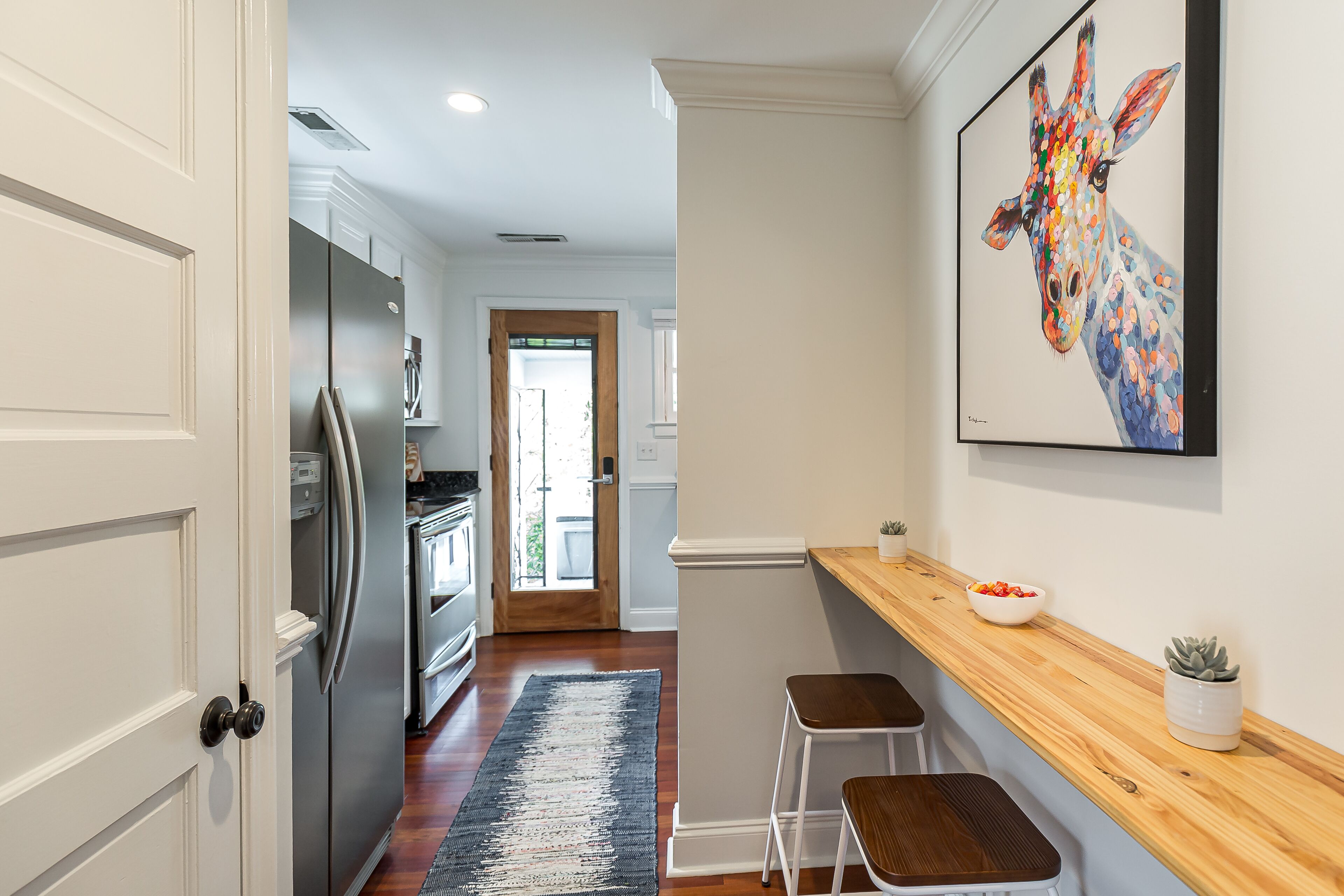A modern kitchen with white cabinetry, a stainless steel refrigerator, and a wooden countertop with two stools.