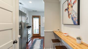 A modern kitchen with white cabinetry, a stainless steel refrigerator, and a wooden countertop with two stools.