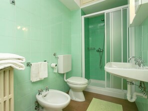 A bathroom with green tiles, a toilet, bidet, sink, and a shower enclosure.