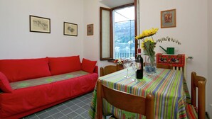 Uma sala de estar acolhedora com um sofá vermelho, uma mesa de jantar de madeira com toalha de mesa colorida e vista para uma montanha através de uma grande janela.