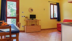 A small, bright room with yellow walls, a wooden table with chairs, a TV on a wooden stand, a red chair, and a window with curtains. - Cozy Cottage in Portomaggiore near Lake (Portomaggiore)