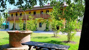 A picnic table in a grassy area with a brick planter and a yellow building with a balcony in the background. - Cozy Cottage in Portomaggiore near Lake (Portomaggiore)