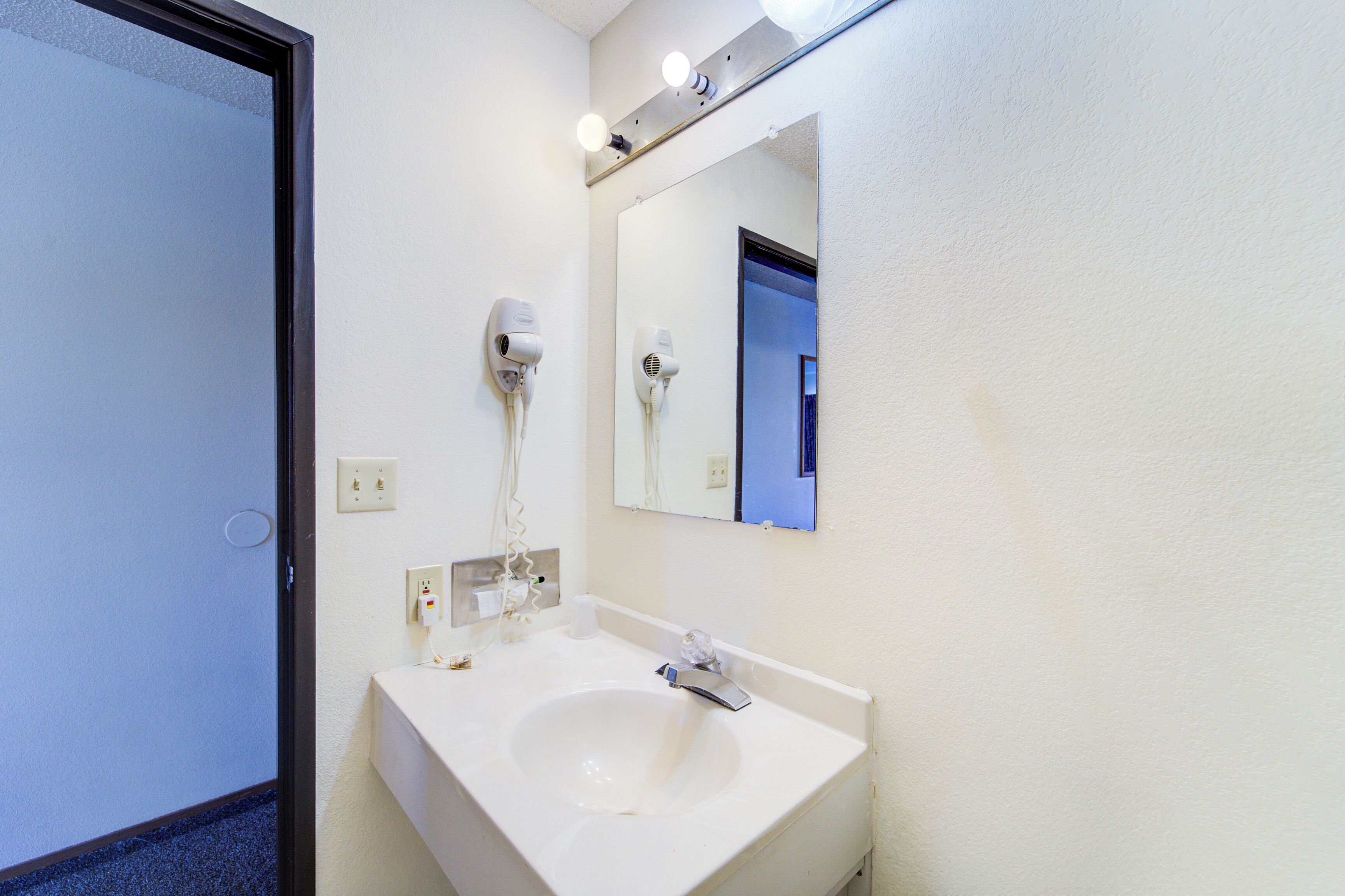 A bathroom with a white sink, a mirror, and two hair dryers mounted on the wall.