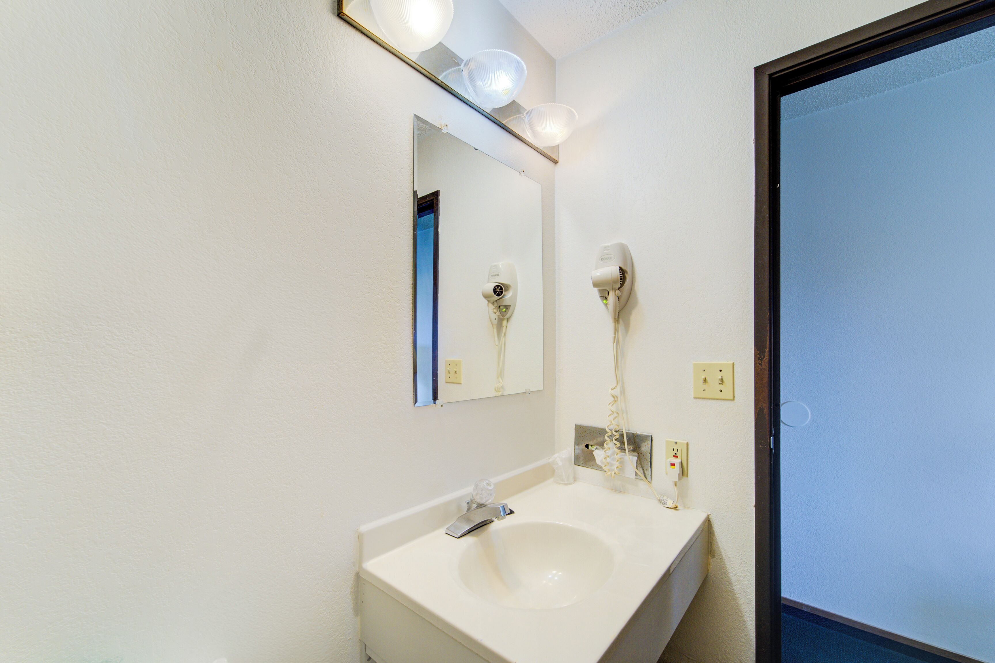 A bathroom with a white sink, a mirror, and two hair dryers mounted on the wall.