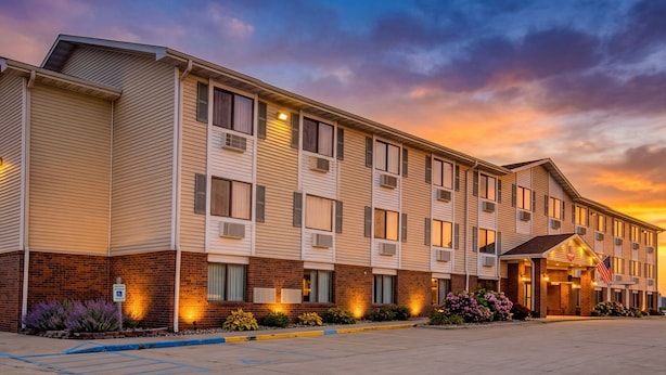 A multi-story hotel with a brick facade, large windows, and an American flag. - Capital O Amerihost Inn and Suites Kingdom City Hwy 54 MO (Kingdom City)