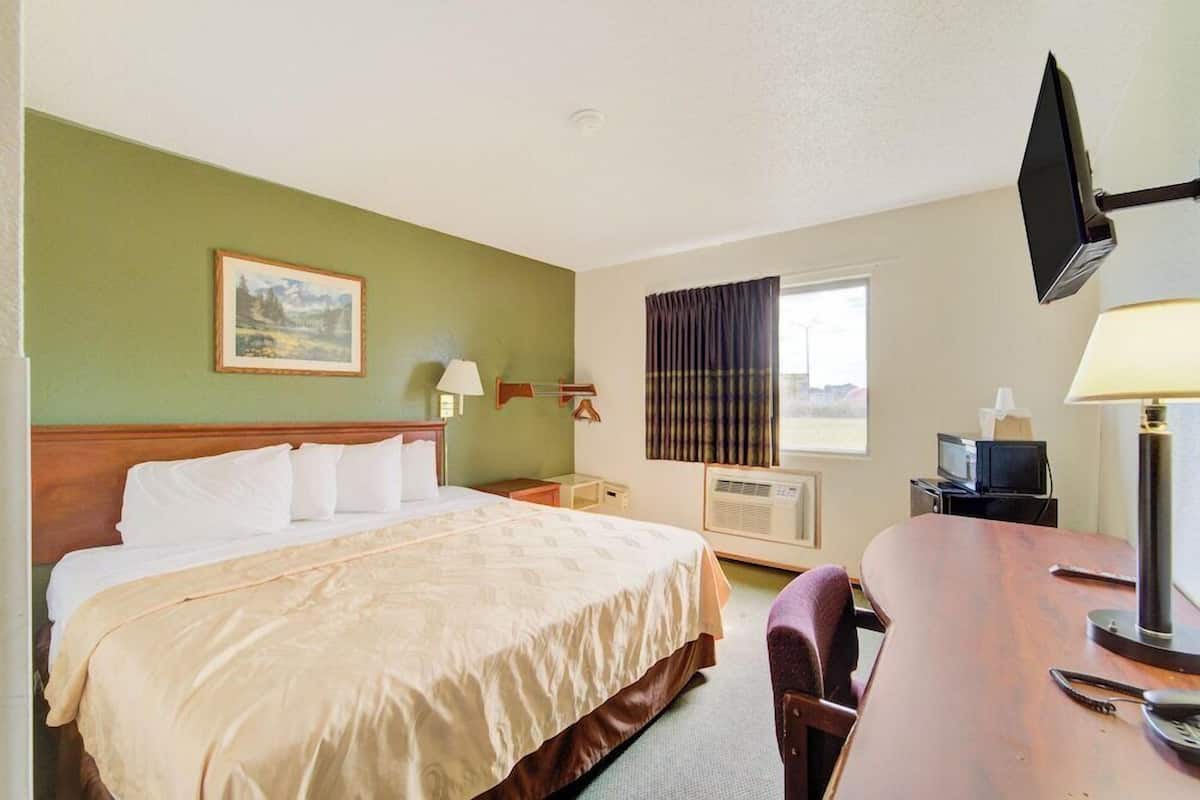 A hotel room with a bed, a desk, a television, a lamp, and a picture on the wall.