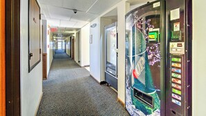 A hotel hallway with a vending machine, carpeted floor, and framed pictures on the walls. - Capital O Amerihost Inn and Suites Kingdom City Hwy 54 MO (Kingdom City)