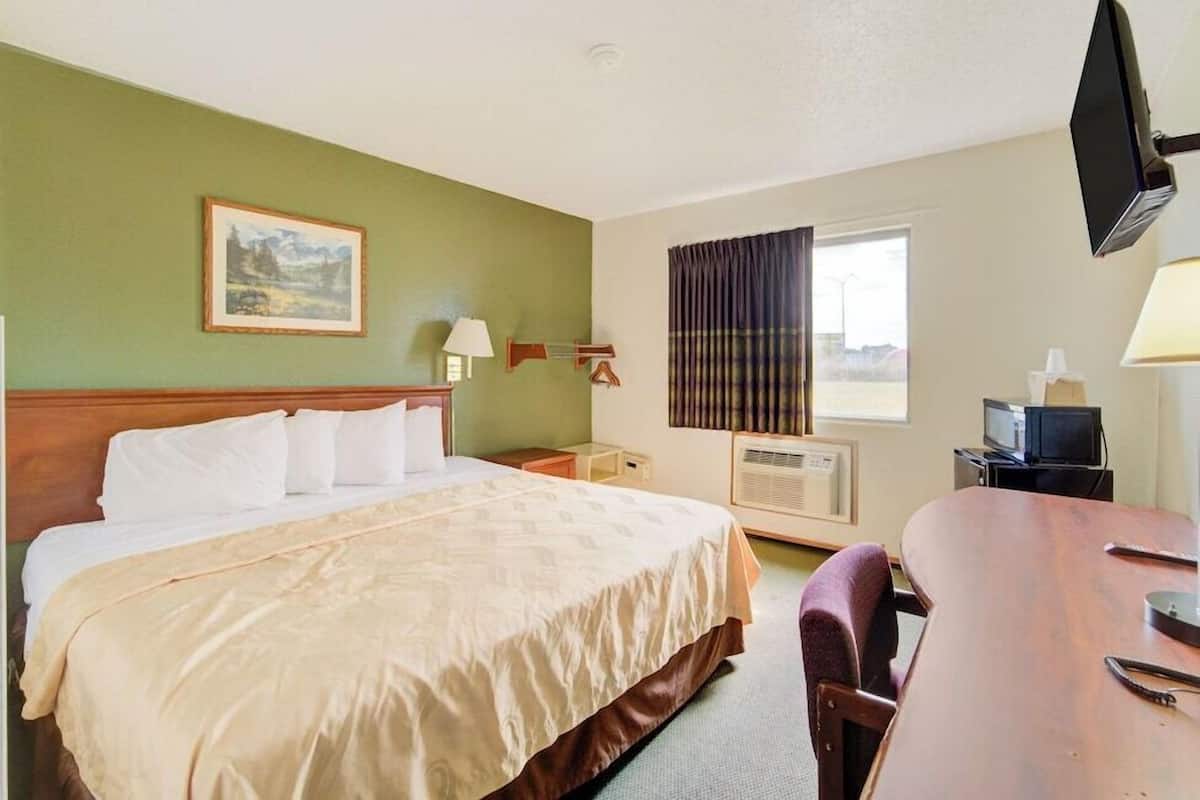 A hotel room with a bed, a desk, a television, and a window with curtains.