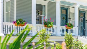 A porch with white balustrades and green doors, adorned with flower baskets. - Luxurious Private Suites in Downtown Charleston (Charleston)