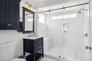 Um banheiro moderno com toucador escuro, vaso sanitário branco, box de vidro e um espelho grande.