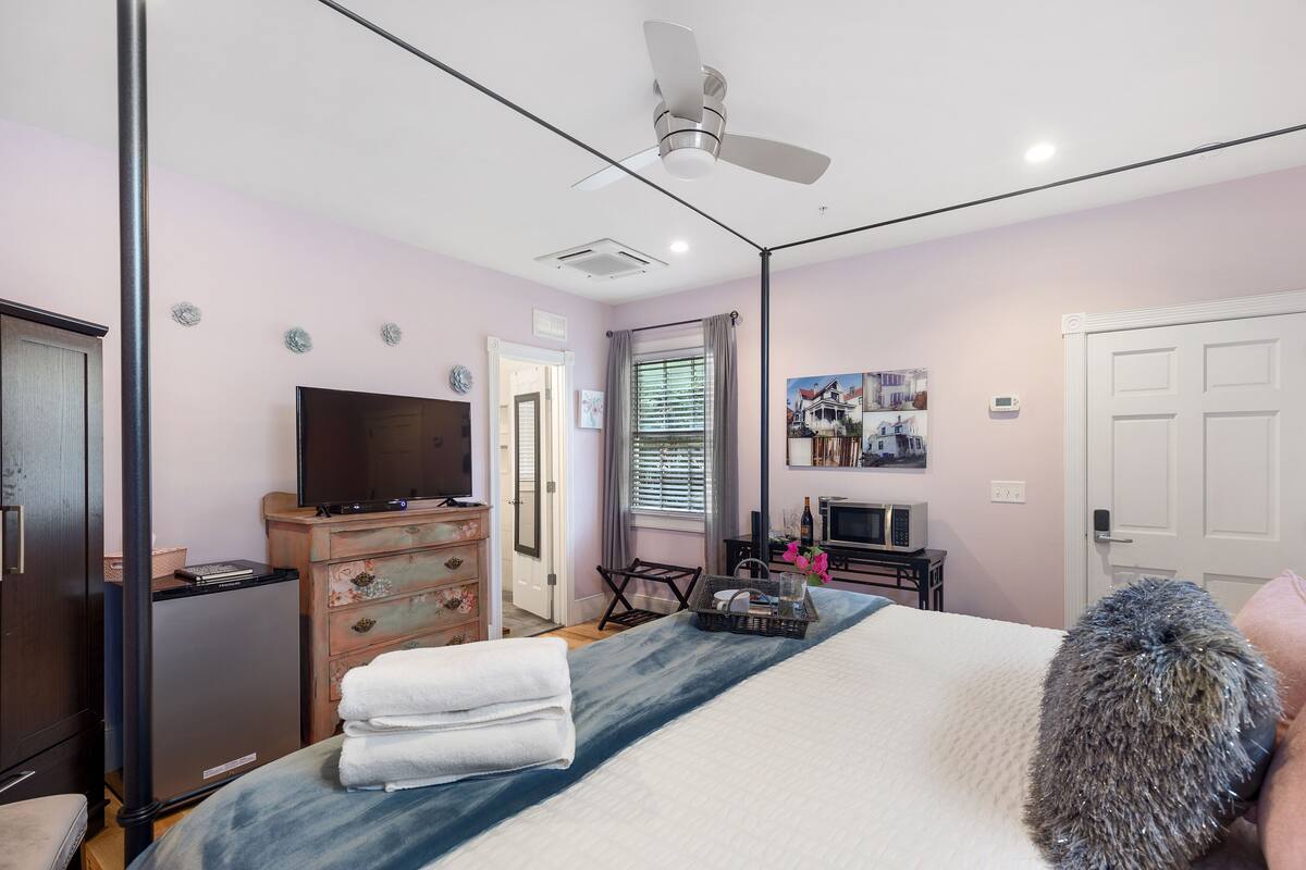 A bedroom with a bed, a television, a dresser, a ceiling fan, and a door.