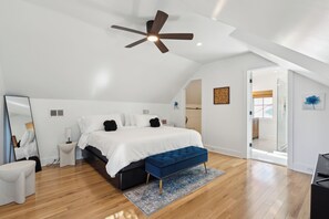 Um quarto com uma cama, um banco azul, um ventilador de teto e piso de madeira.
