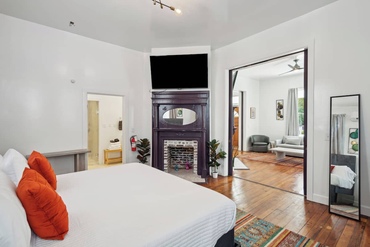 A modern bedroom with a large bed, a fireplace, a television, and a mirror.