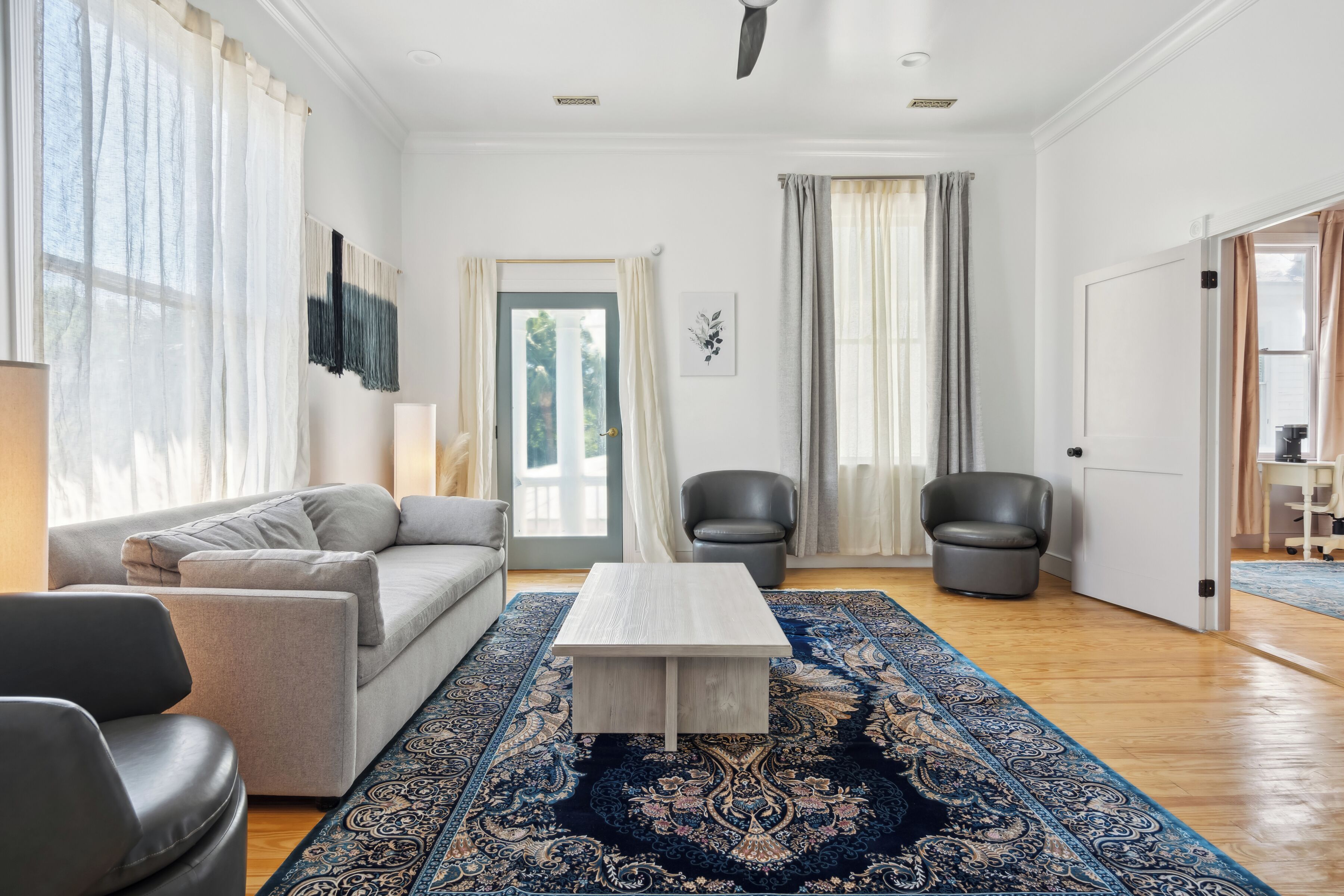 A spacious living room with a sofa, two armchairs, a coffee table, and a large rug.