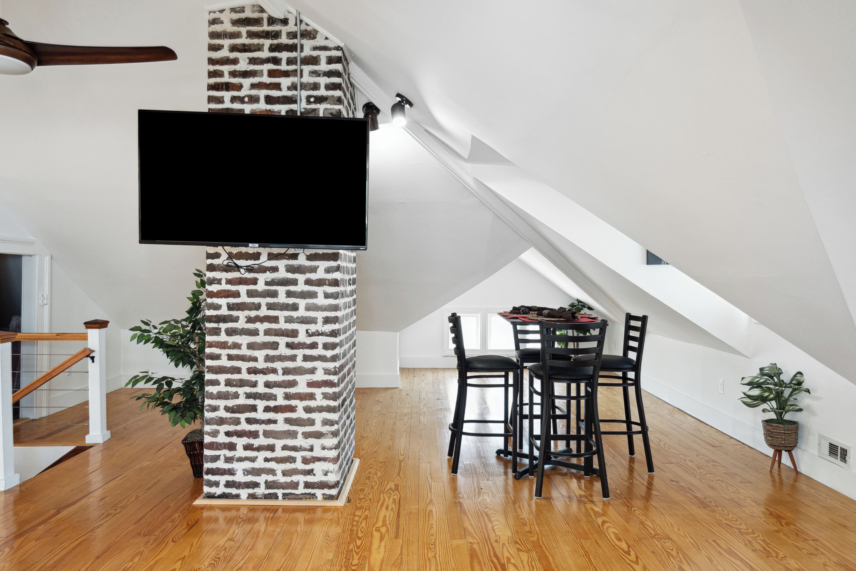 Ein modernes Loft mit einer Ziegelwand, einem Flachbildfernseher, einem Essbereich mit Holzboden und einer Treppe.