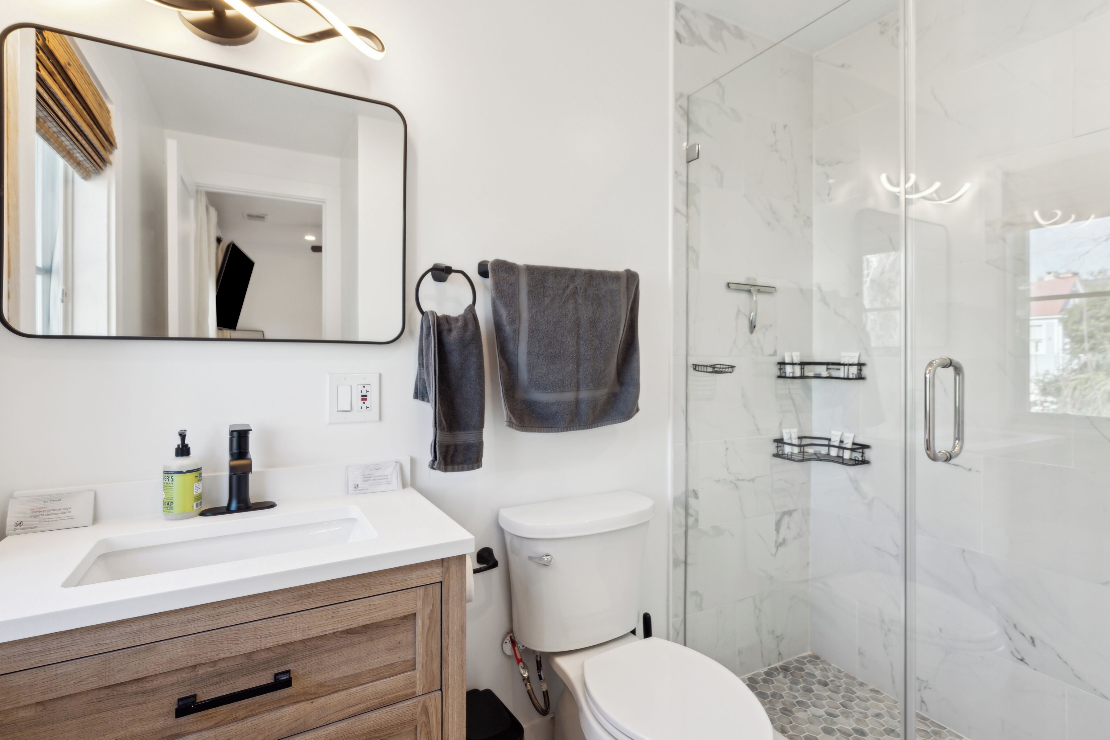 A modern bathroom with a white sink, wooden vanity, a toilet, and a glass shower enclosure.