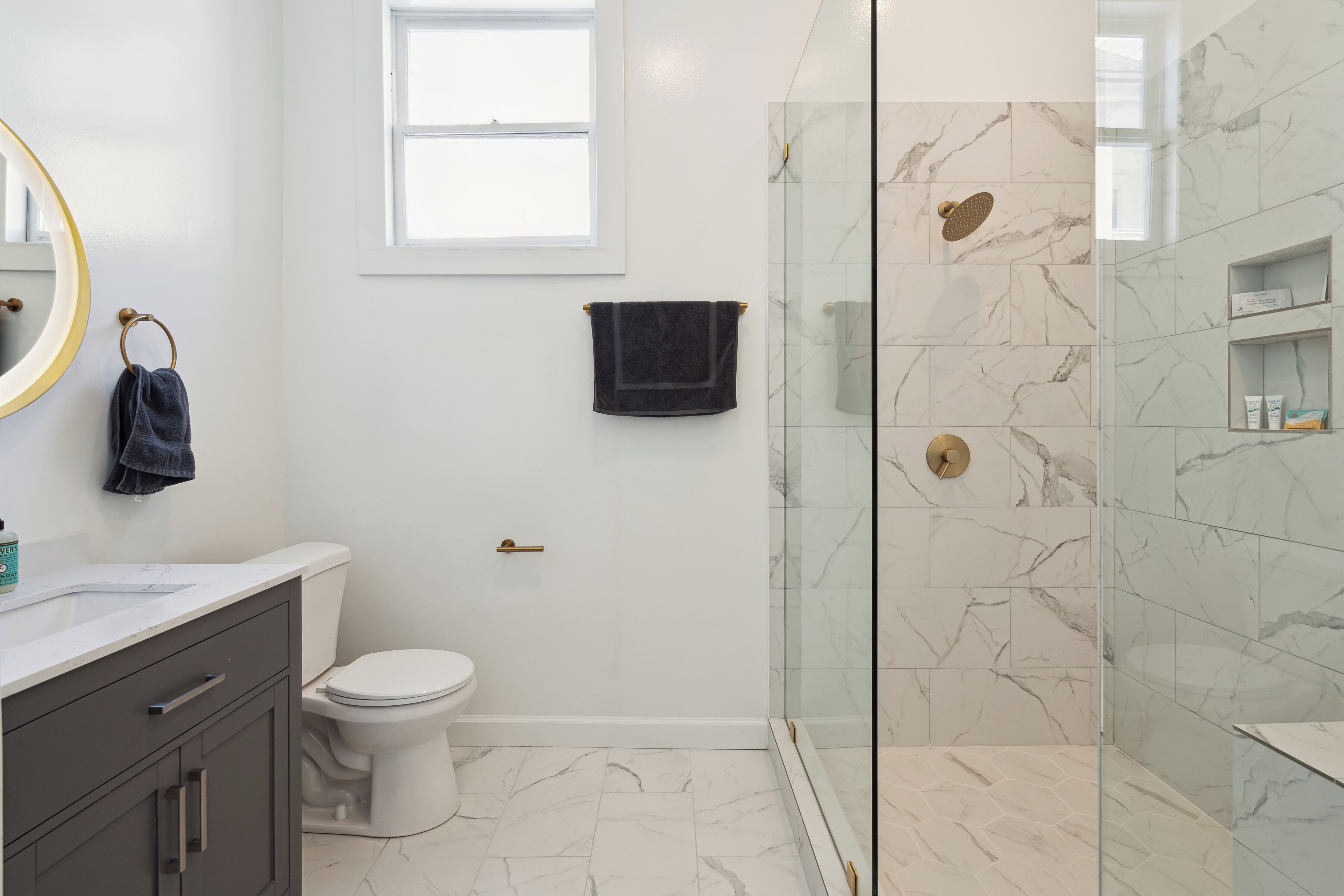 A modern bathroom with a glass-enclosed shower, a white toilet, and a marble-tiled floor.