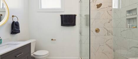 A modern bathroom with a glass-enclosed shower, a white toilet, and a marble-tiled floor.