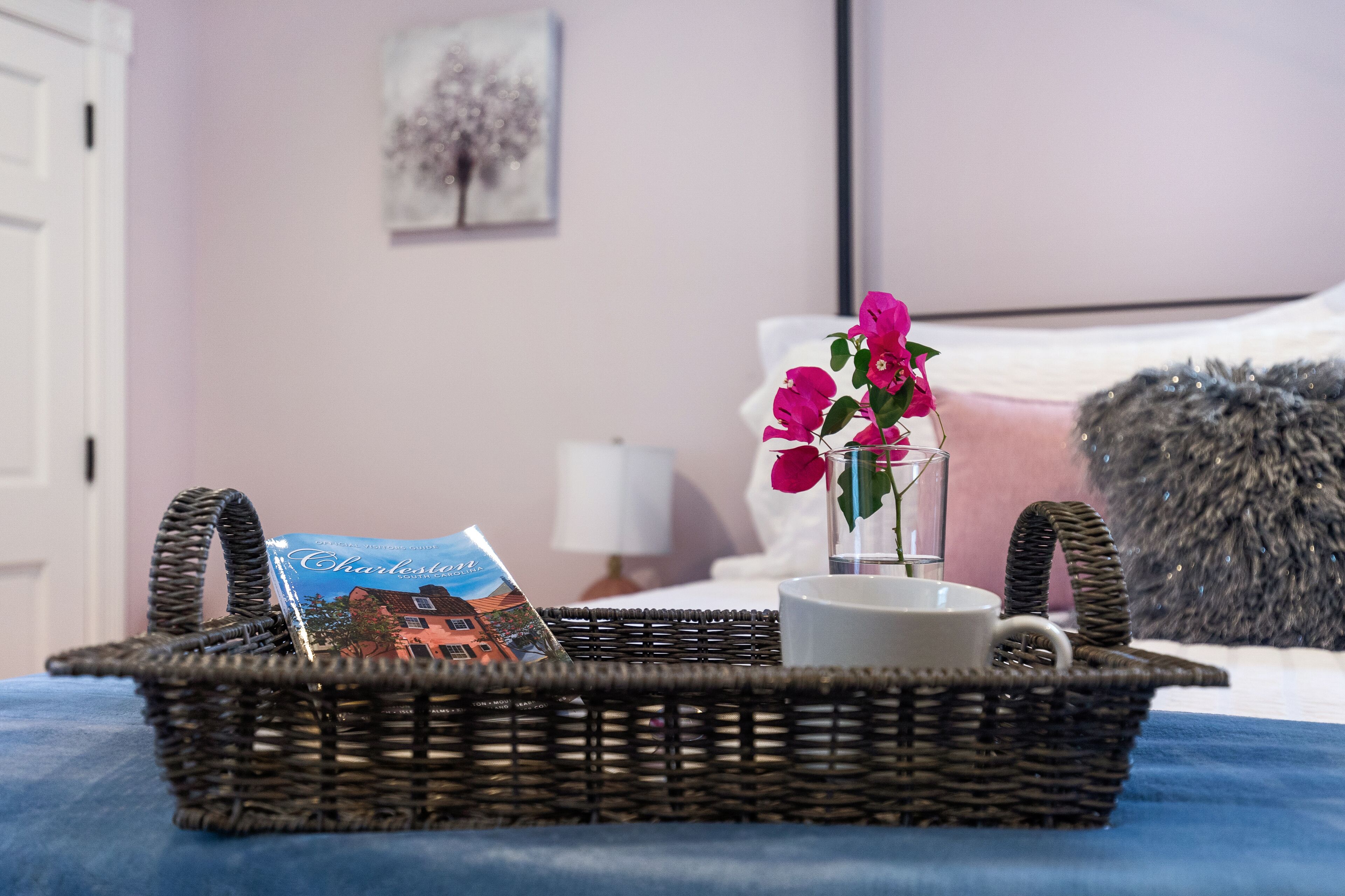 A wicker basket with a book, a mug, and a vase with flowers on a bed.