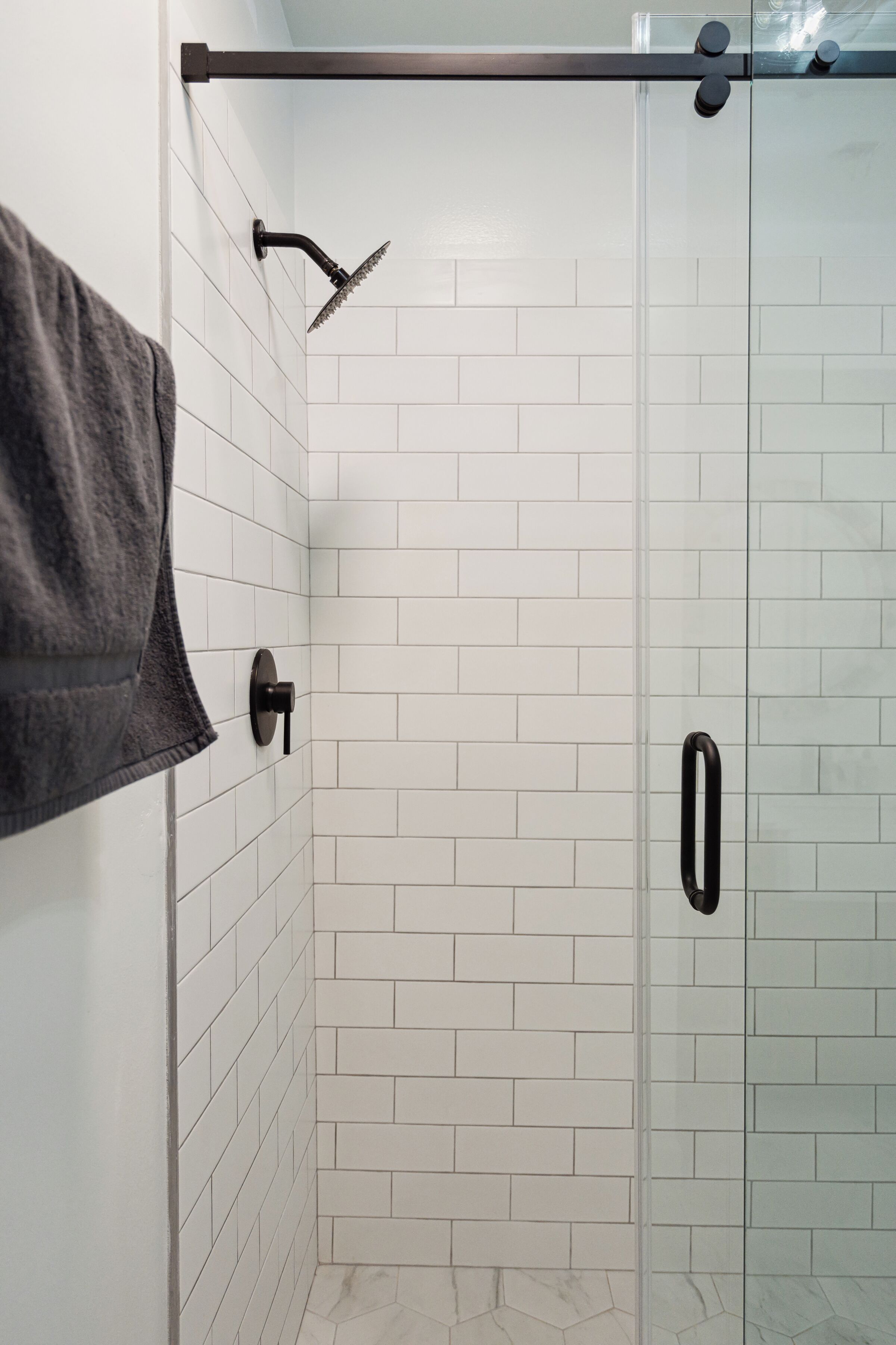 A glass-enclosed shower with white tiles and a towel hanging on the wall.