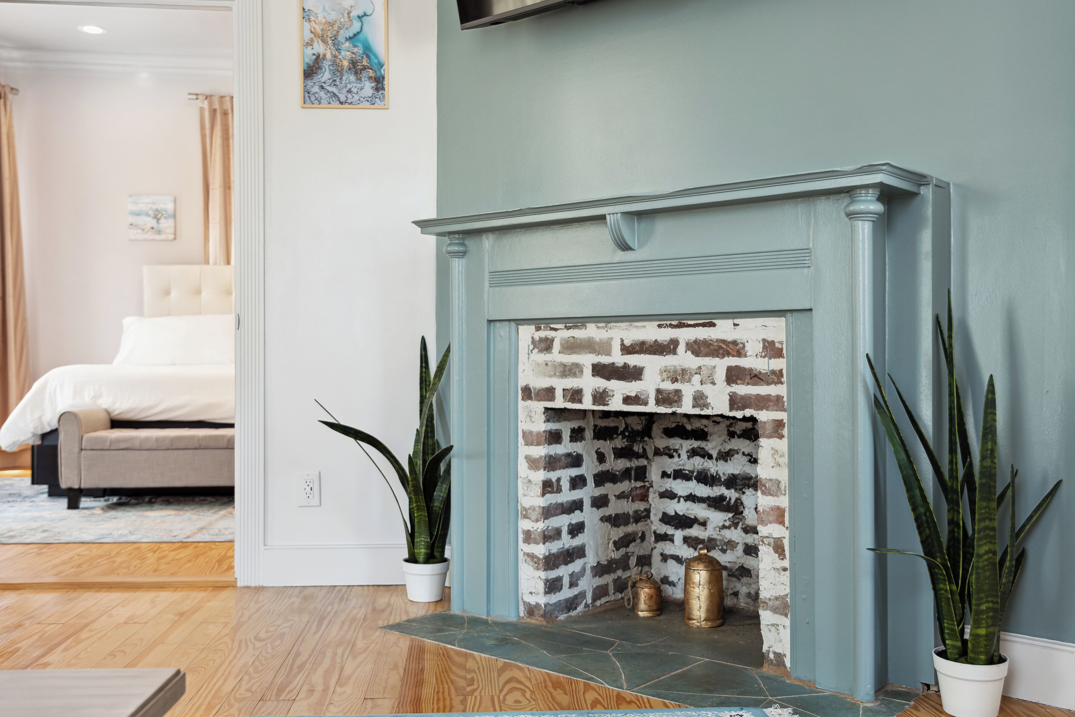 A room with a brick fireplace, a bed, and two potted plants.