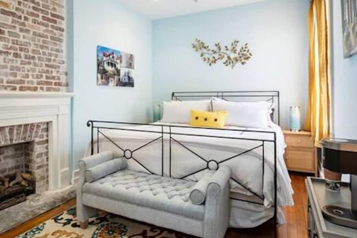 A bedroom with a bed, a fireplace, a sofa, and a decorative wall piece.