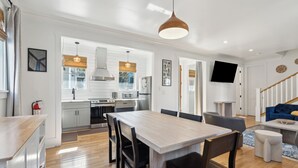 A modern kitchen with white cabinets, a dining area with a wooden table and chairs, a living room with a blue sofa, and a staircase with wooden railings. - Luxurious Private Suites in Downtown Charleston (Charleston)