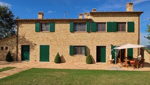 A two-story stone building with green shutters, a brick patio, and outdoor seating. - Cottage in Montelabbate With Pool & Forest (Montelabbate)