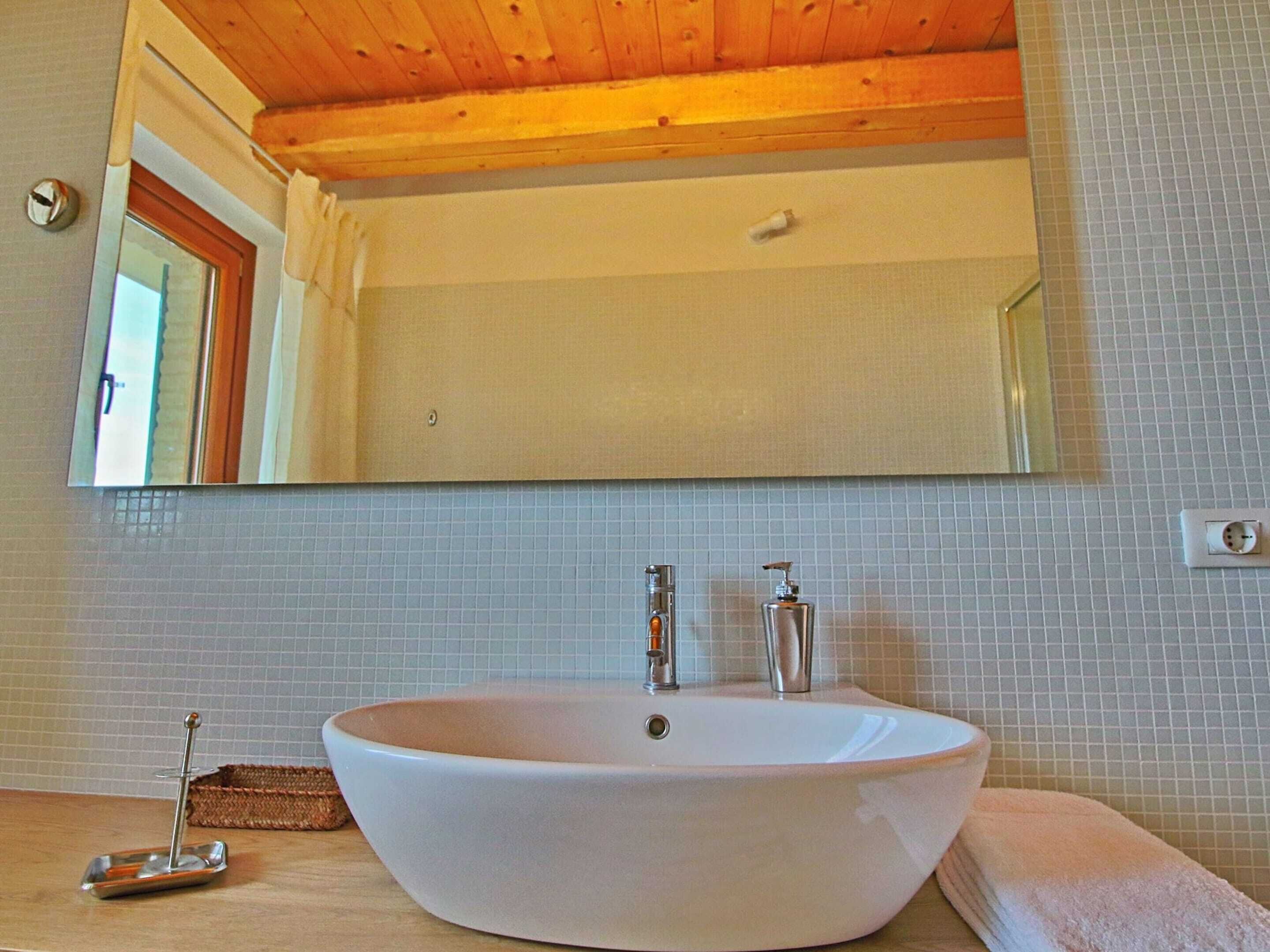 A bathroom with a large oval sink, a mirror above it, and a wooden ceiling.