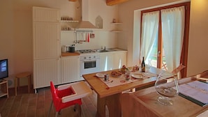 A compact kitchen with white cabinets, a stove, and a sink. There's a dining table with chairs, a small stool, and a TV on a stand. - Cottage in Montelabbate With Pool & Forest (Montelabbate)