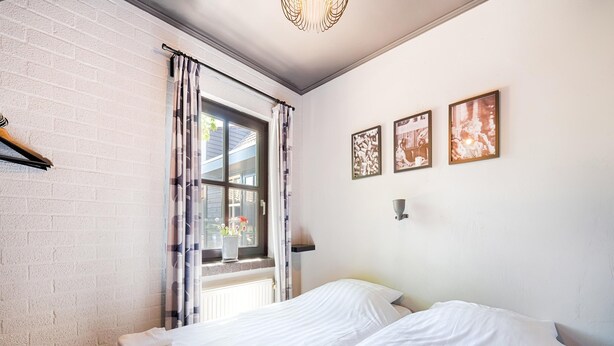 Slaapkamer met twee bedden, een raam met gordijnen, een radiator en wanddecoratie.