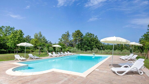 Uma piscina retangular com um deck revestido, rodeada por espreguiçadeiras e guarda-sóis brancos.