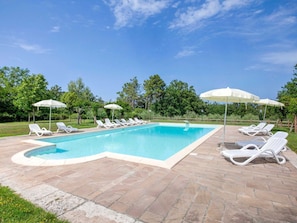 A rectangular swimming pool with a tiled deck, surrounded by white lounge chairs and umbrellas.