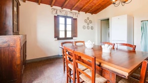 Uma sala de jantar com mesa e cadeiras de madeira, um candelabro, uma janela com persianas e um radiador.