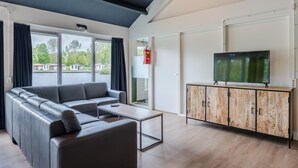 A modern living room with a sectional sofa, a coffee table, and a TV on a wooden cabinet. - Well Furnished Home for Groups with Dishwasher near Water (Gasselternijveen)