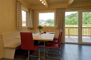 A wooden dining area with a table set for two, red chairs, and a view of a house through a window. - Pleasant Chalet With Sauna (Murau)