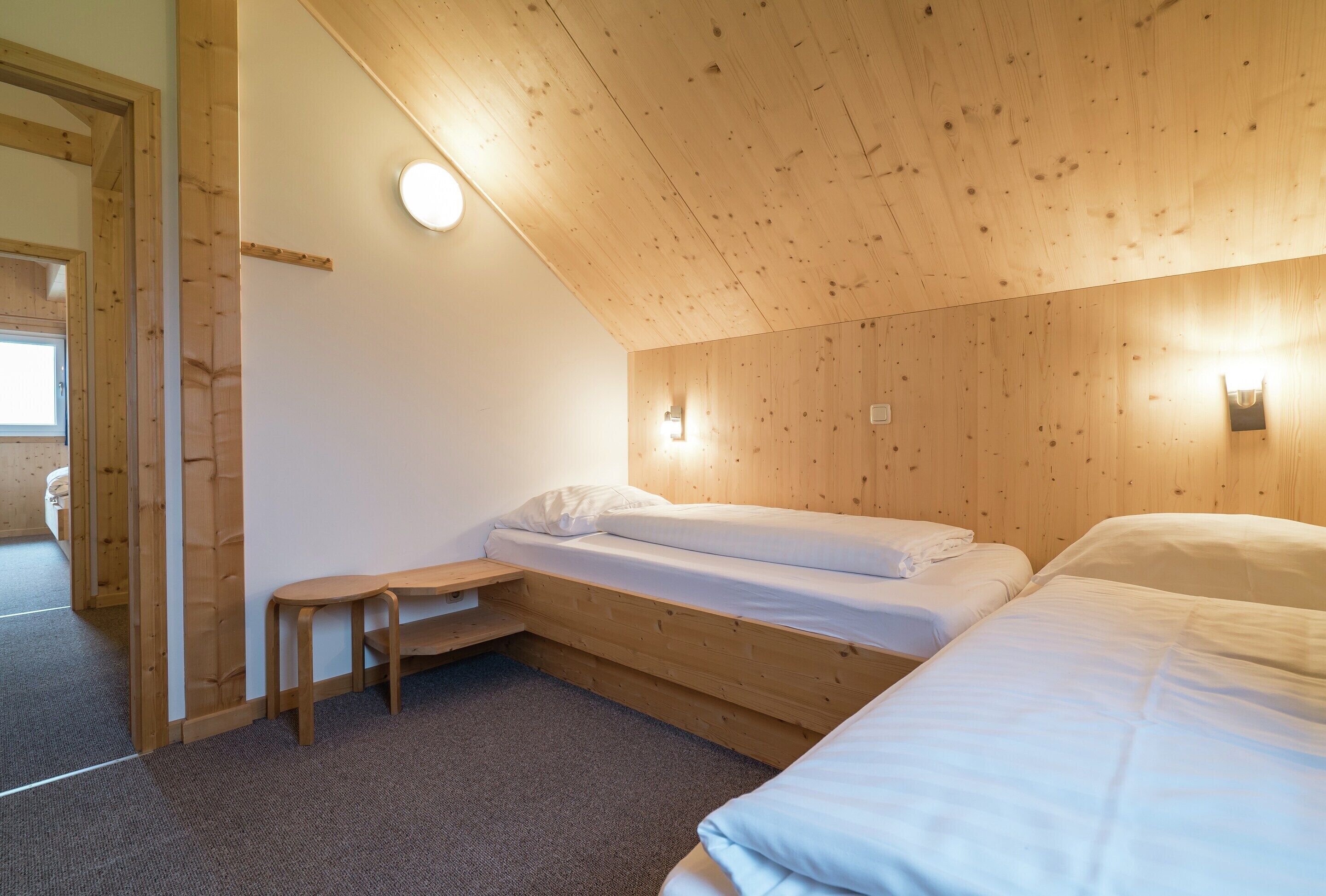 A small, cozy room with a sloped ceiling, wooden walls, and a single bed.