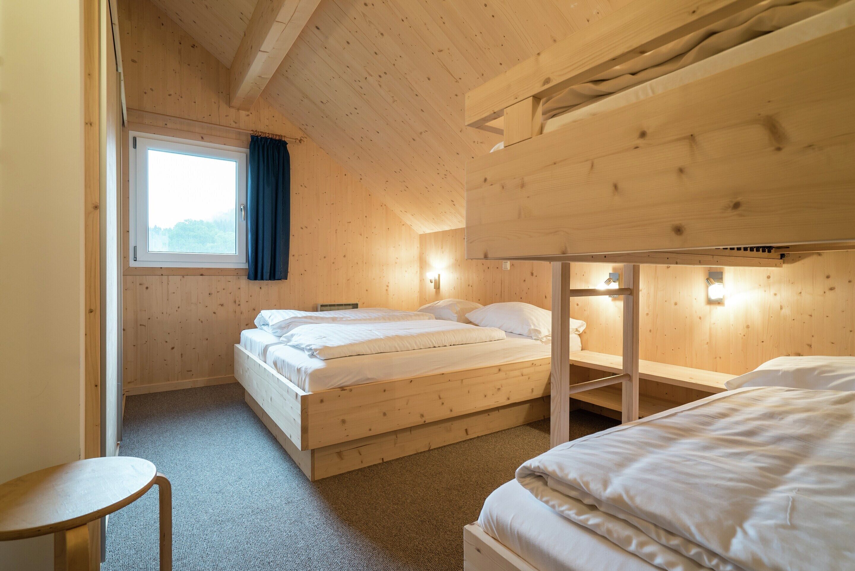 A wooden cabin room with bunk beds, a window with curtains, and a small table.