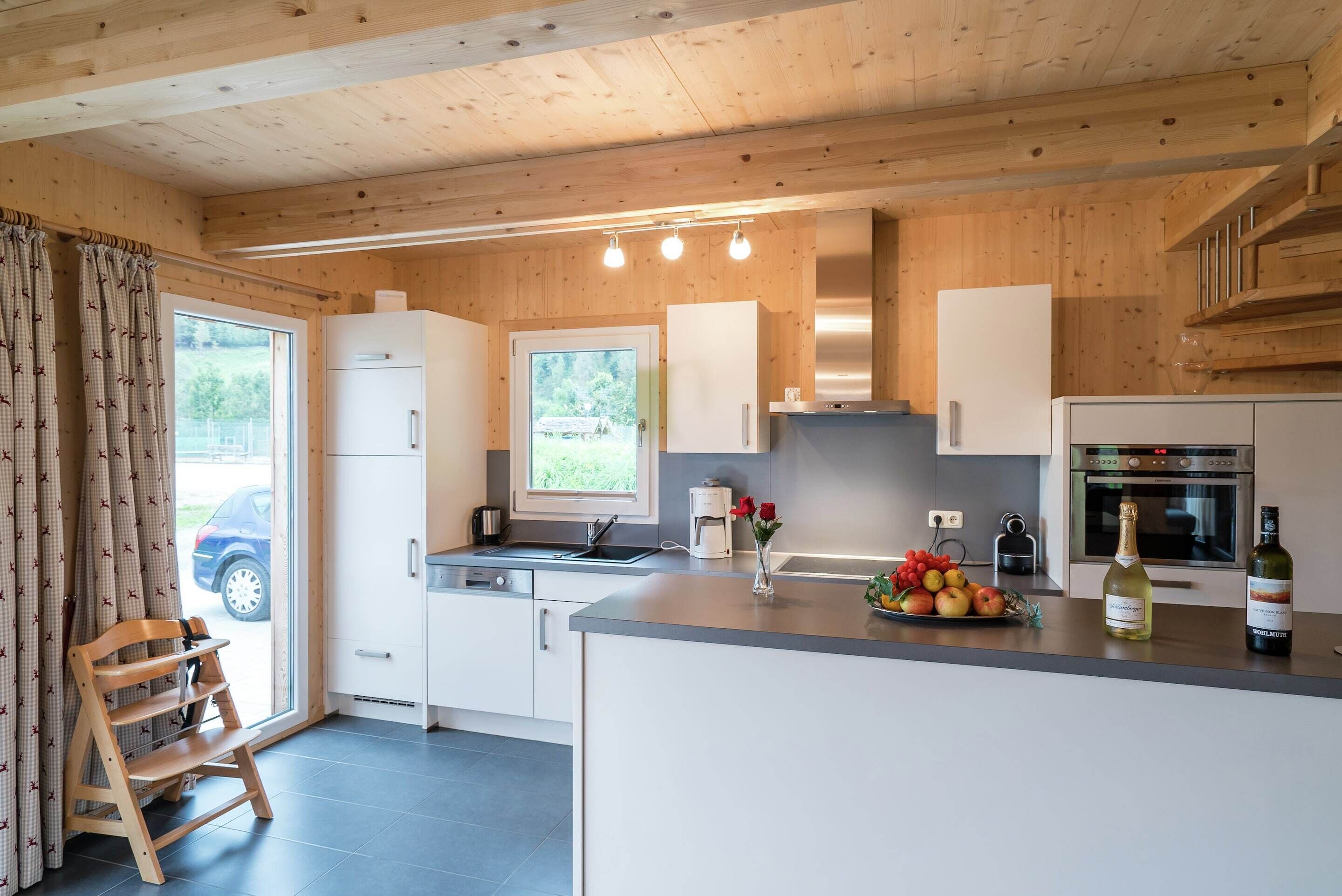 A modern kitchen with wooden cabinets, a built-in oven, and a large island with a fruit bowl and wine bottles.