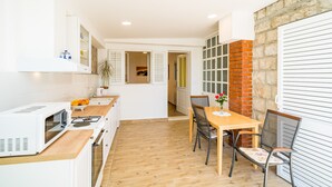 Une cuisine compacte avec des meubles blancs, un four à micro-ondes et une cuisinière. On y trouve une table à manger en bois, des chaises et une plante en pot.