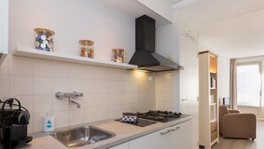 A modern kitchen with a gas stove, stainless steel sink, and white cabinets. There are jars on a shelf above the stove and a coffee machine on the counter. - Apartment in Zoutelande Near Sandy Beach (Zoutelande)