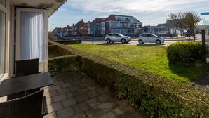 A residential area with a paved patio, a wicker chair, and a view of houses and parked cars. - Apartment in Zoutelande Near Sandy Beach (Zoutelande)