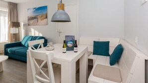 A modern living room with a white sofa, teal cushions, a white dining table, and a pendant light. - Apartment in Zoutelande Near Sandy Beach (Zoutelande)