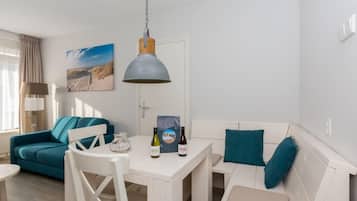 Een moderne woonkamer met een witte bank, kussens in teal-tint, een witte eettafel en een hanglamp.