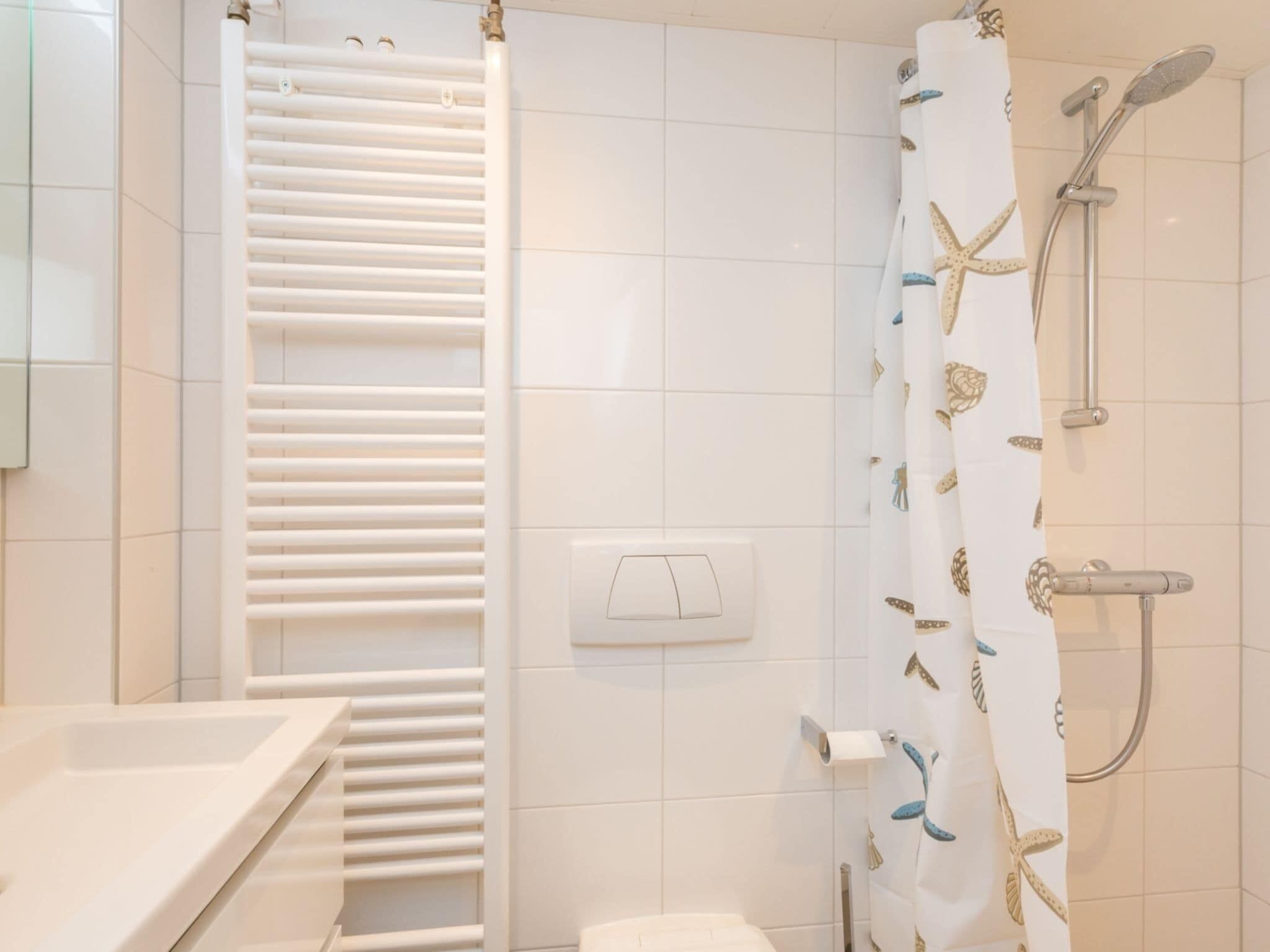 Een badkamer met een witte betegelde muur, een witte handdoekhouder, een douche met een gordijn met sterren en een toilet.