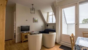Um quarto acolhedor com televisão, sofá, mesa de jantar e janela com cortinas.